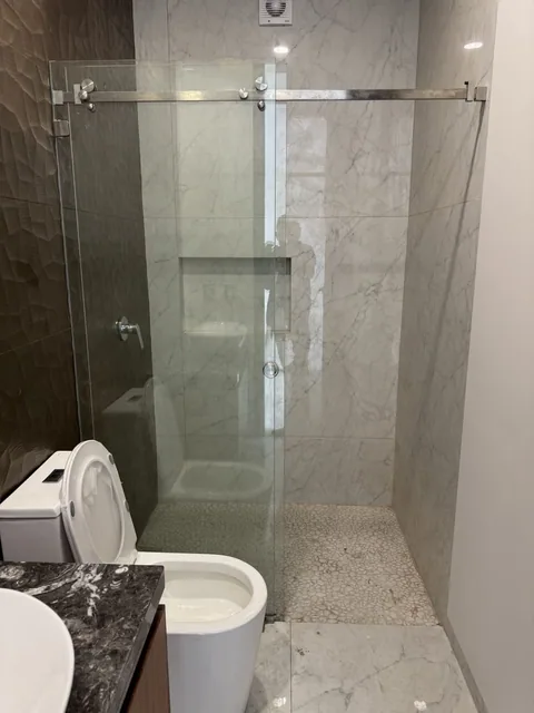 Cancel de baño de cristal templado con puerta corrediza sobre muro de mármol